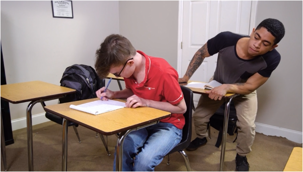 He gets up and walks over to Tony's desk to read his answers